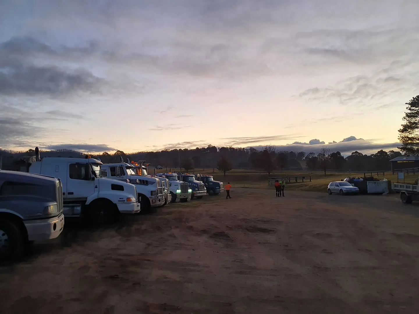 Parked trucks at dawn with people nearby.